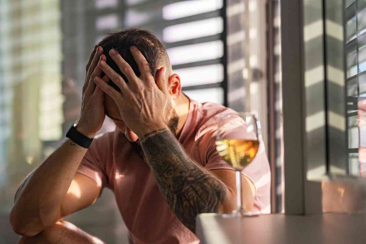 Person experiencing stress and alcohol dependence sitting near a glass of alcohol