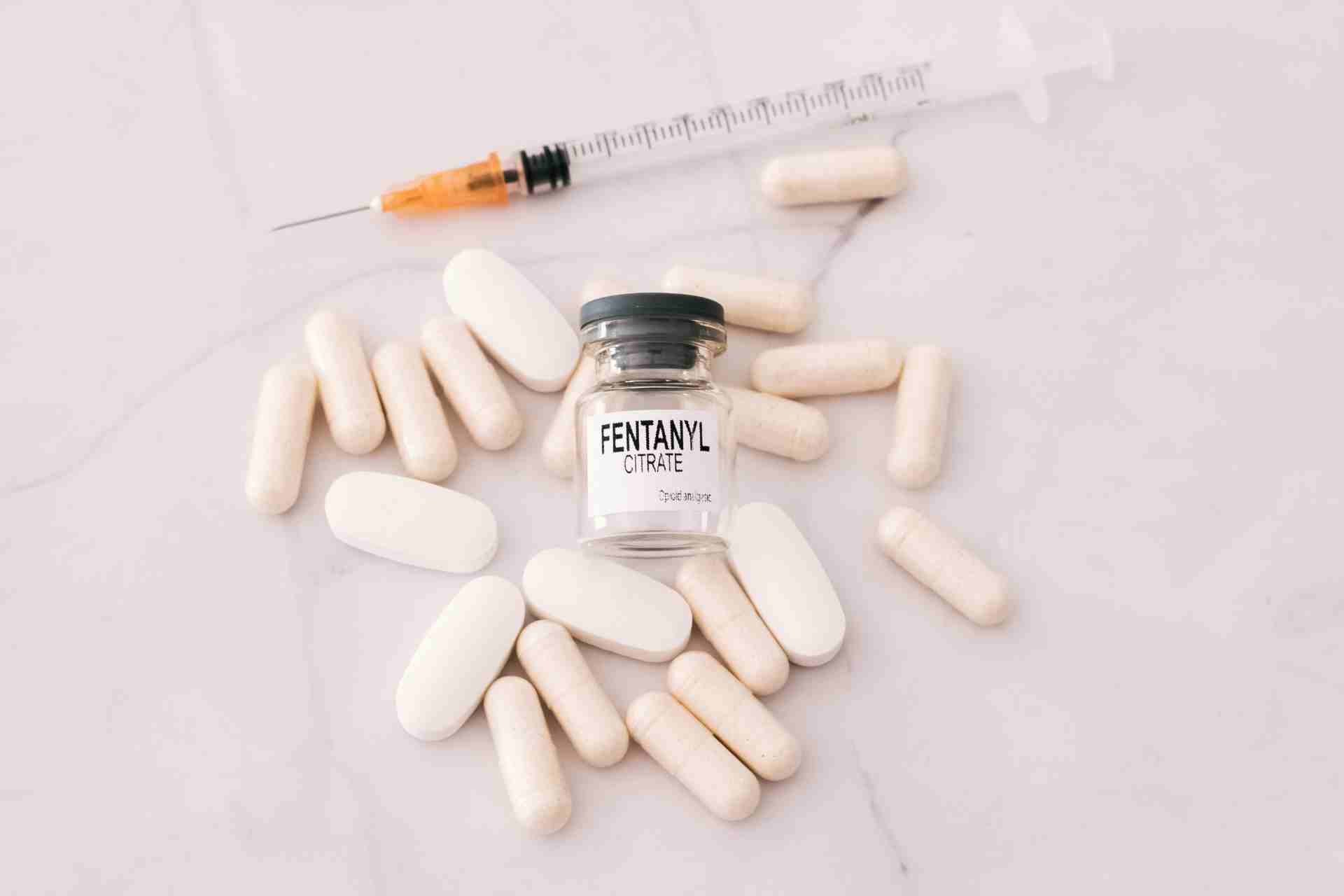 Vial labeled fentanyl citrate surrounded by pills and a syringe illustrating the dangers of fentanyl addiction and overdose