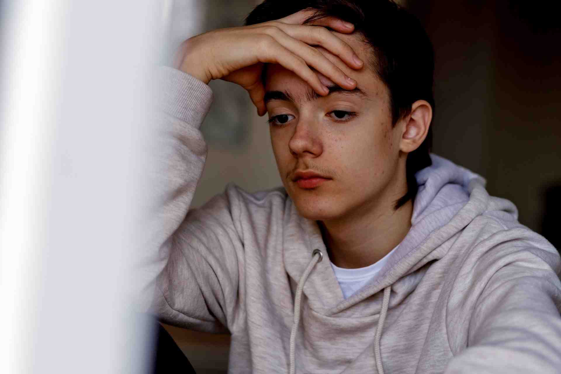 Teen sitting with hand on forehead while looking stressed during a substance abuse evaluation
