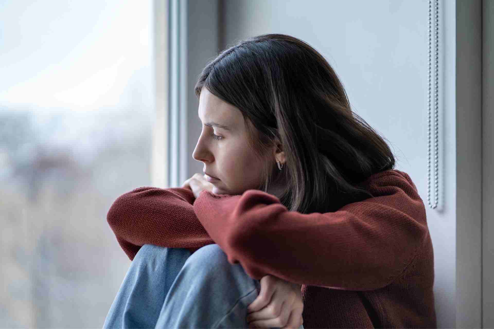 Woman sitting alone by a window reflecting on the emotional effects of alcohol on mental health.